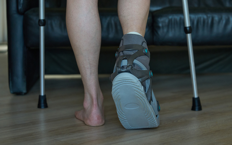 Patient using crutches and orthopedic boot for high ankle recovery.