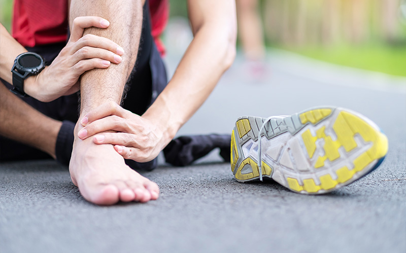 Athlete sitting on a gym floor holding their injured bare ankle.