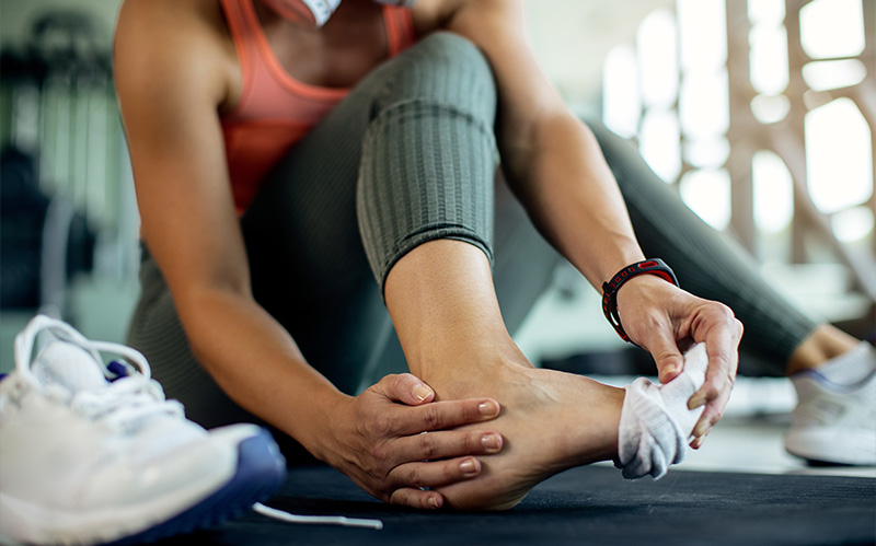 Athlete sitting on a gym floor holding their injured bare ankle.