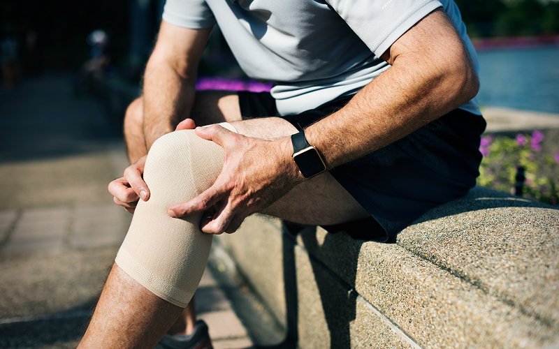 Runner holding painful inner knee wrapped in compression sleeve.